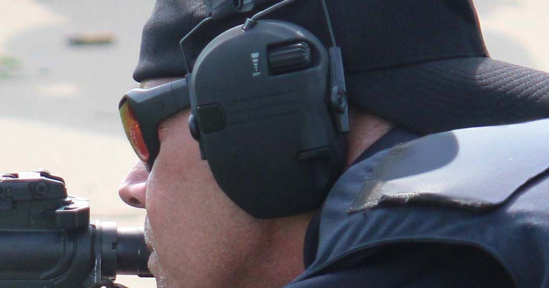 Person holding a rifle with a scope and wearing a tactical headset.