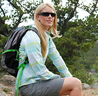 woman sitting on a rock wearing a backpack and popticals sunglasses 
