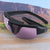 pink and black popticals sunglasses in front of a lake 
