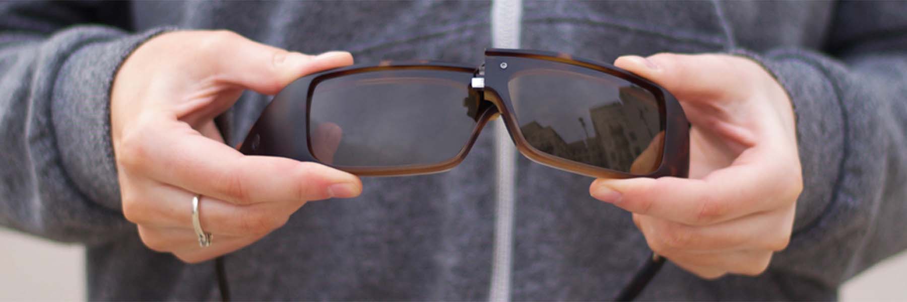 Close-up of a hand holding a pair of Popticals sunglasses, showcasing NYDEF® Optics