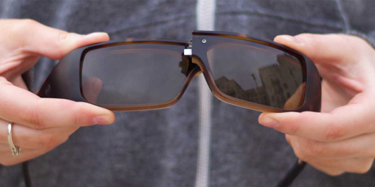 Close-up of a hand holding a pair of Popticals sunglasses, showcasing NYDEF® Optics
